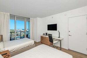 A hotel room with a bed, a desk, a chair, a TV, and a view of the city. - Lovely Studio With Amazing Views (Hallandale Beach)