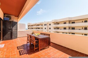 A balcony with a table and chairs, a view of a multi-story building, and an air conditioning unit. - Iberlagos Casa Luna Sea View Dona Ana Beach (Lagos)