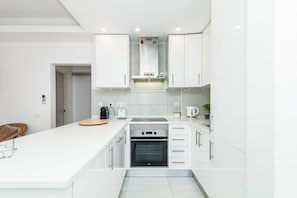 A modern kitchen with white cabinetry, a built-in oven, and a countertop with a kettle and toaster. - Iberlagos Casa Luna Sea View Dona Ana Beach (Lagos)