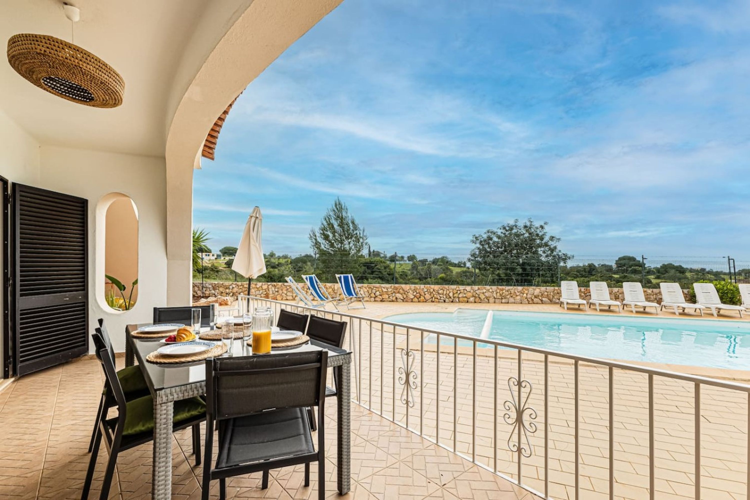 An outdoor dining area with a pool, chairs, and a view of the landscape.