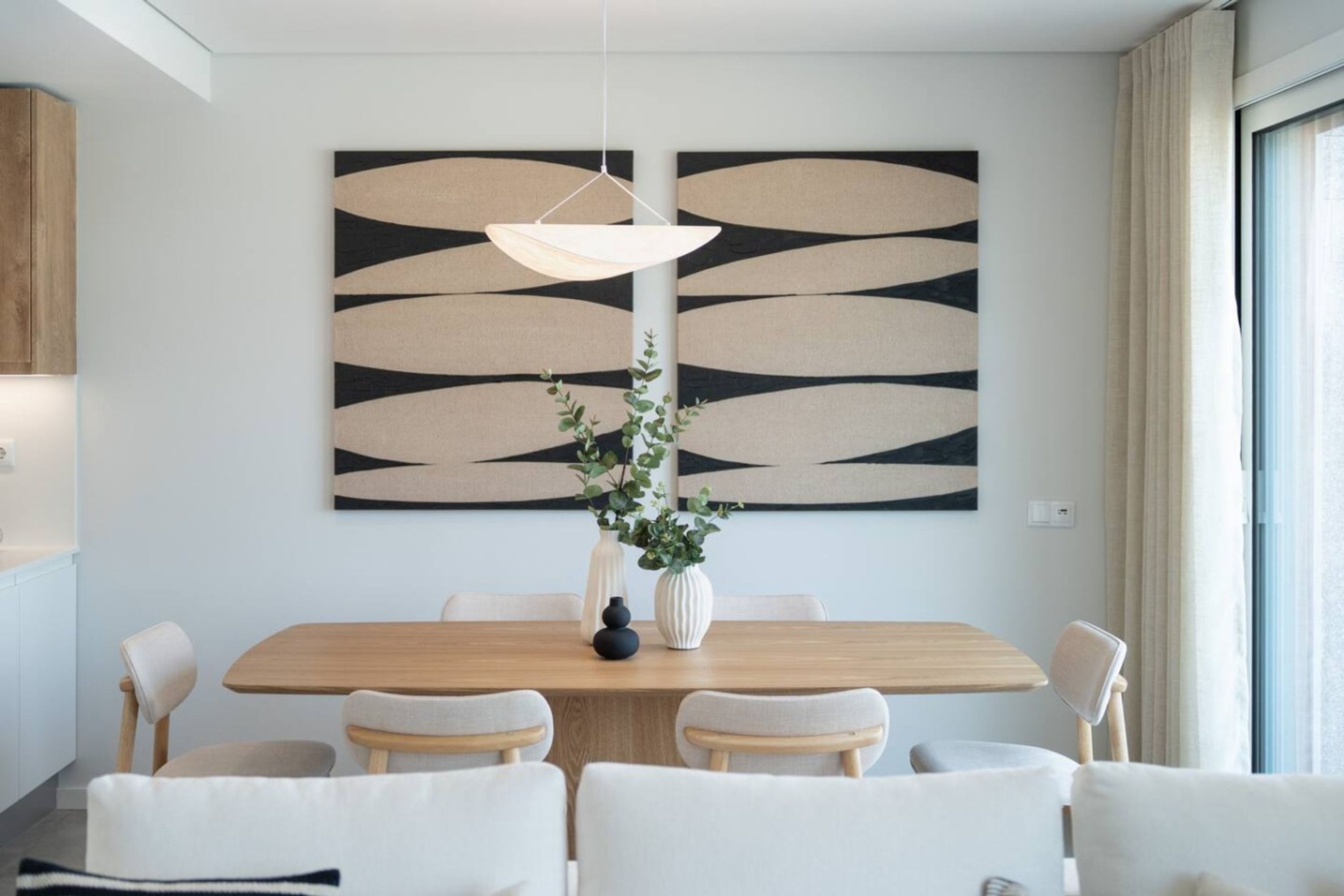 A modern dining area with a wooden table, white chairs, and a central vase with greenery.