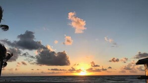 A beach scene with a sunset, ocean, and a structure on the right. - Beachside Comfort 2BR and 2BA With Outdoor Dining (Hollywood)