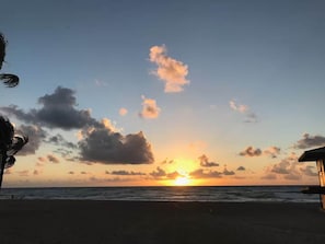 Een strandscène met een ondergaande zon, zee en een gebouw aan de rechterkant.