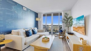 Ein modernes Wohnzimmer mit einem großen Fenster, einem Sofa, einem Couchtisch und einem Gemälde von einer Strandansicht.