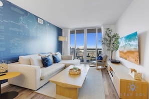 Ein modernes Wohnzimmer mit einem großen Fenster, einem Sofa, einem Couchtisch und einem Gemälde von einer Strandansicht.