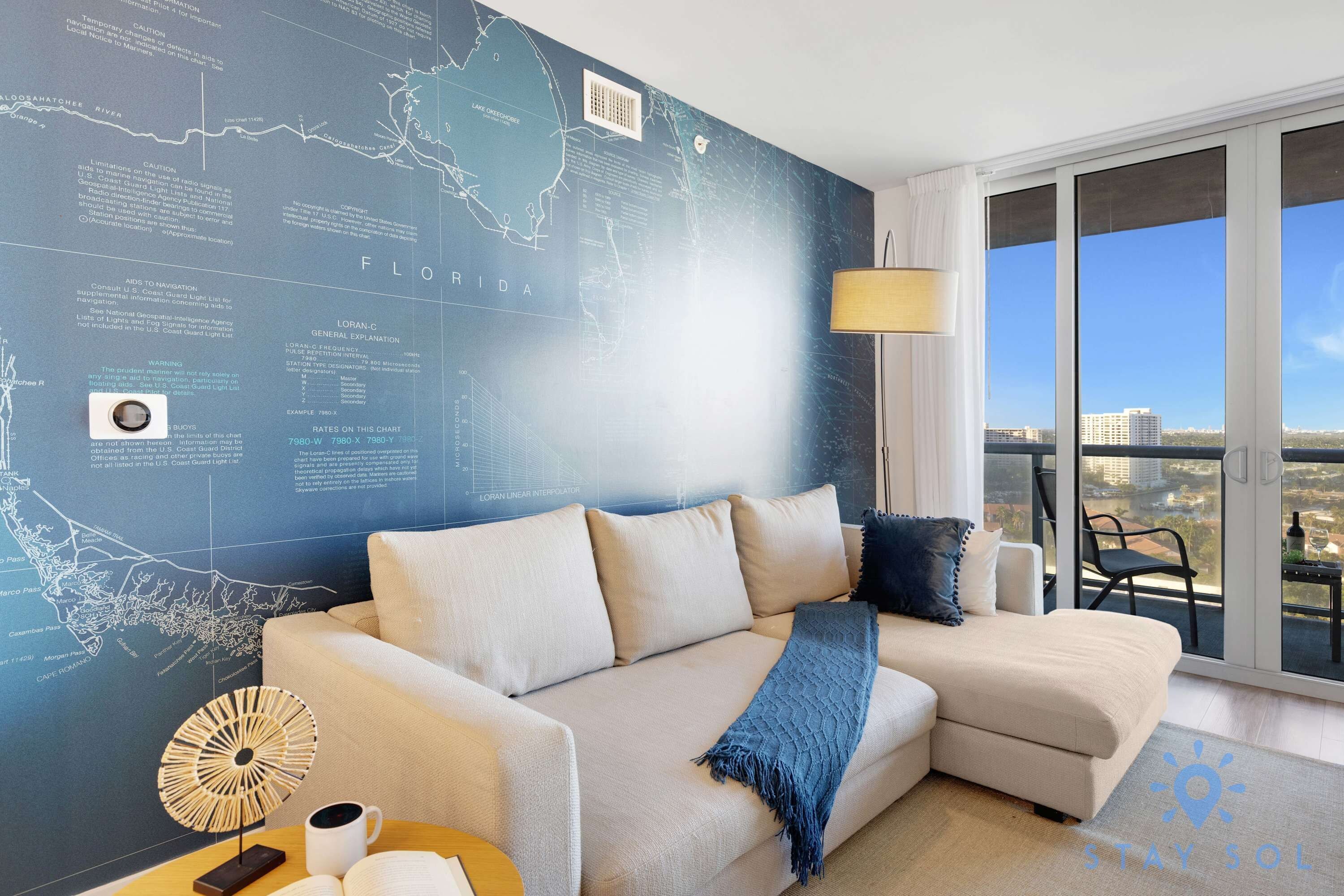 Ein modernes Wohnzimmer mit einer großen Wandkarte, einem Sofa, einem Couchtisch und Blick auf die Stadt vom Balkon aus.