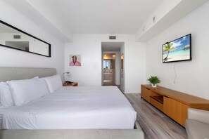 A modern hotel room with a large bed, a wooden console, a TV, and a bathroom visible through an open door. - Top Luxury Apartment With Pool Gym (Hallandale Beach)