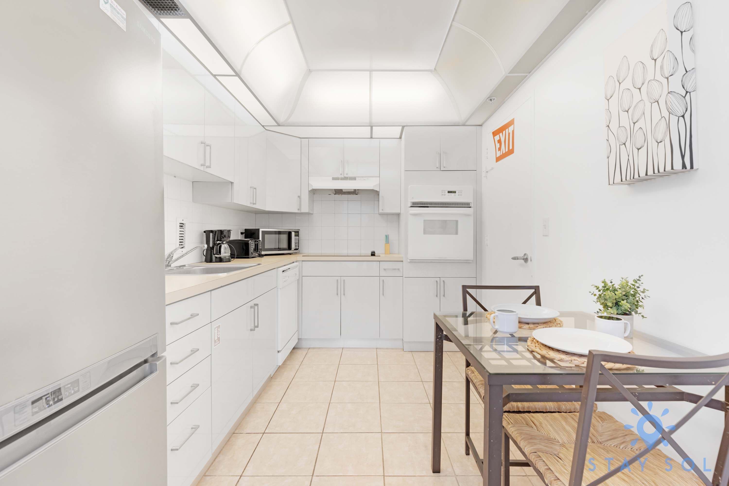 A modern kitchen with white cabinets, a microwave, a coffee maker, and a dining area with a table and chairs.