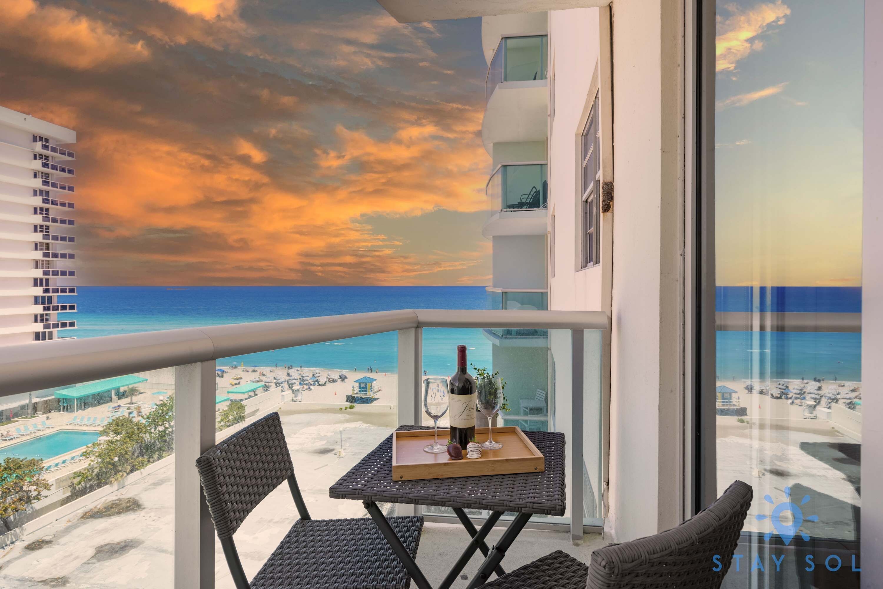A balcony with a table set for two, overlooking a beach and ocean.