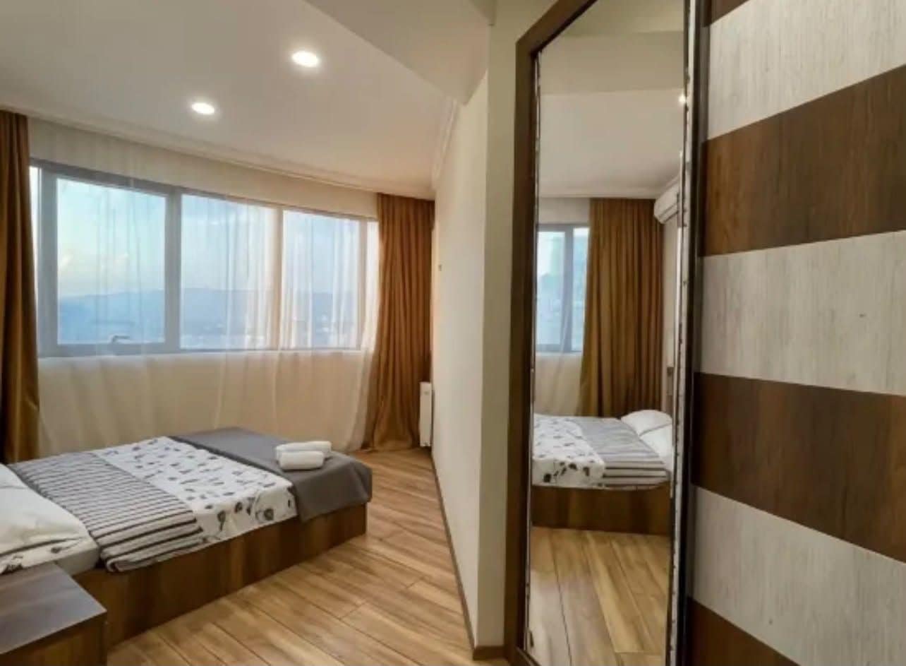 A hotel room with two beds, a large mirror, and a view of the city.