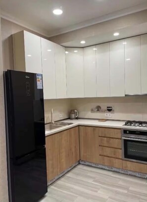 A modern kitchen with white cabinets, a black refrigerator, wooden cabinets, a sink, a kettle, and a stove. - GREAT APARTMENT IN THE CENTER OF TBILISI (T'bilisi)