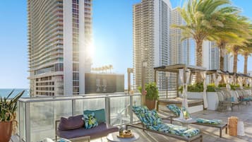 Terraço no telhado com área de estar ao ar livre, vista para o oceano e edifícios altos ao fundo.