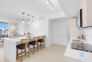 Una cocina moderna con una isla central, taburetes de bar, iluminación colgante y vistas a la ciudad.