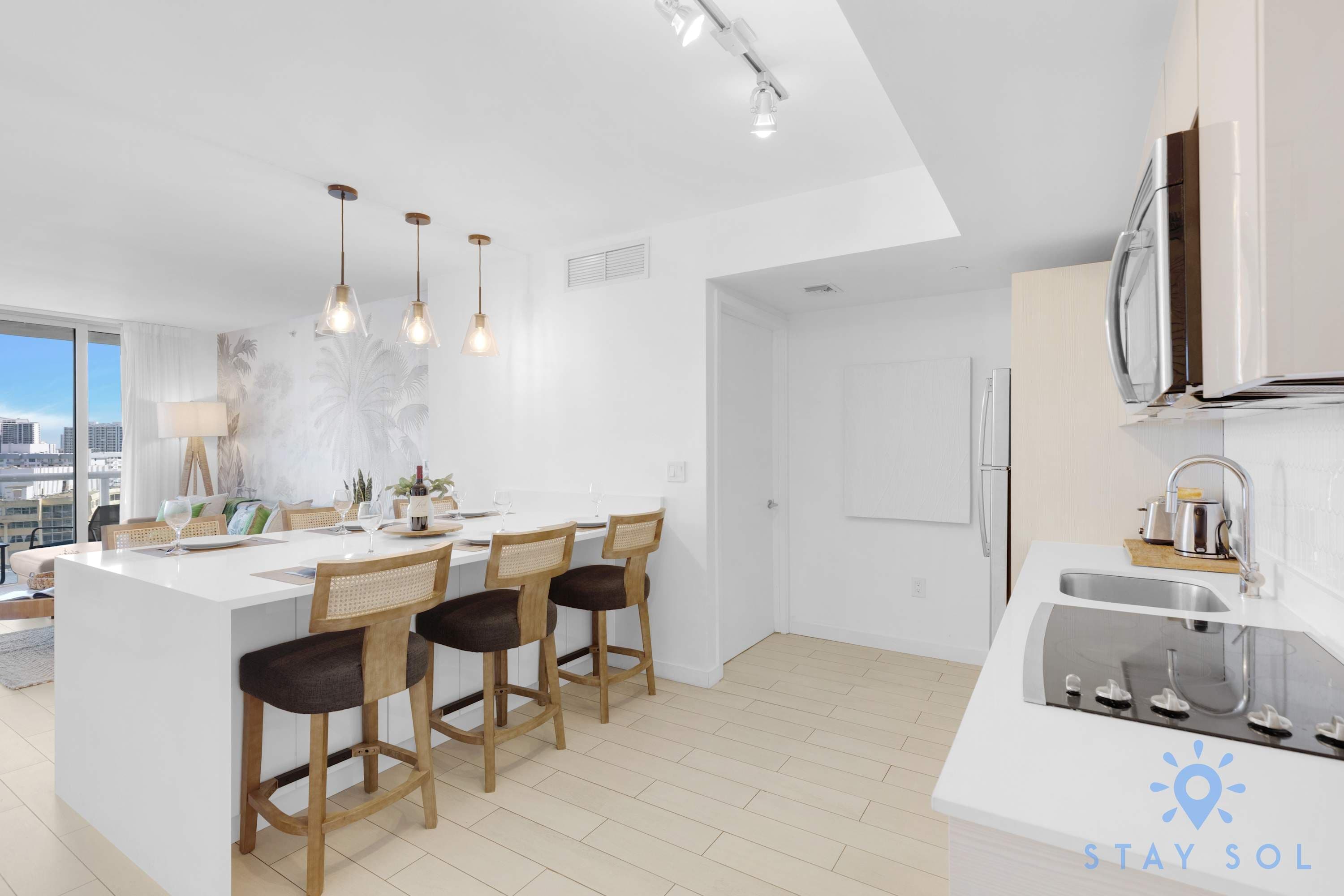 Una cocina moderna con una isla central, taburetes de bar, iluminación colgante y vistas a la ciudad.