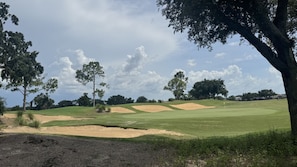 A golf course with sand bunkers, trees, and a clear sky.