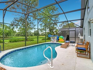 A covered outdoor swimming pool with a clear view of the surrounding landscape, including trees and a distant golf course.