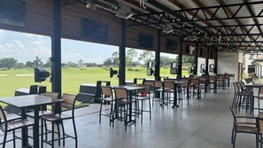Un área de estar interior con mesas y sillas, con vistas a un campo de golf.
