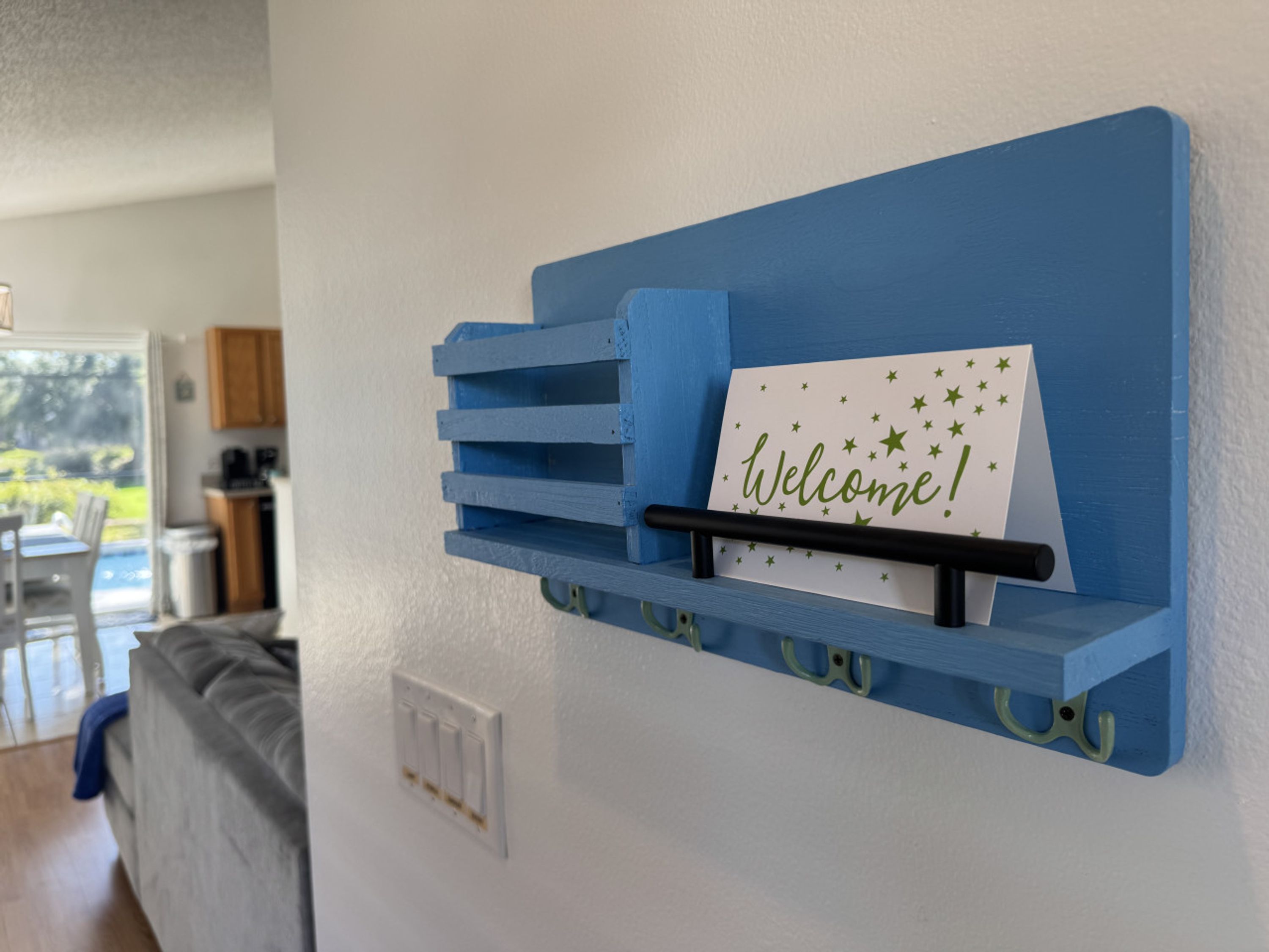 A blue wall-mounted rack with a 'Welcome!' sign and a card with stars.