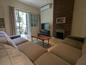 A living room with a sofa set, a television, a fireplace, and a balcony with curtains. - Gladstone Apartment in Nicosia (Nicosia)
