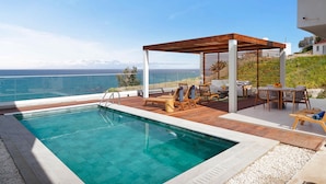 A swimming pool with a wooden deck and lounge chairs, overlooking a body of water with mountains in the distance. - Villa Lara Seafront in Polis (Pachyammos)