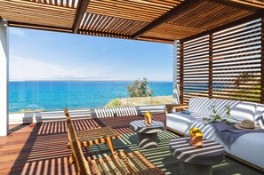 A modern outdoor seating area with a view of the sea, wooden furniture, and a white sofa with cushions. - Villa Lara Seafront in Polis (Pachyammos)