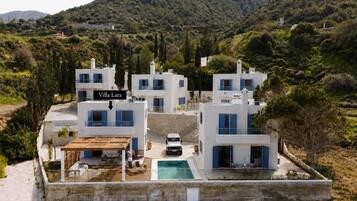 A modern villa complex with a pool, surrounded by lush greenery and hills.