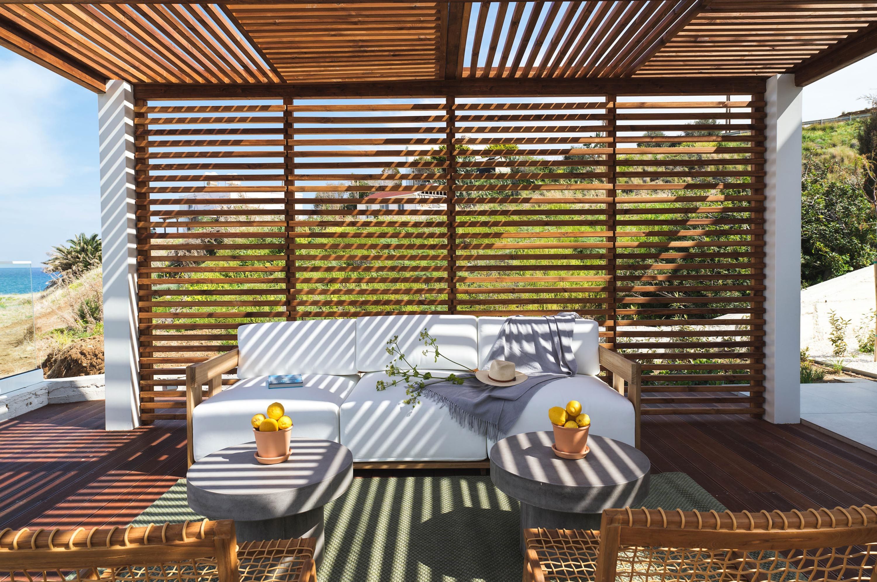 Un área de estar al aire libre techada con un sofá y dos sillones, una mesa, y vistas del paisaje.
