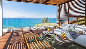 A modern outdoor seating area with a view of the sea, wooden furniture, and a glass balustrade. - Villa Lara Seafront in Polis (Pachyammos)