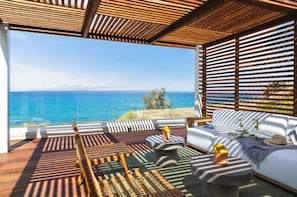 A modern outdoor seating area with a view of the sea, wooden furniture, and a glass balustrade. - Villa Lara Seafront in Polis (Pachyammos)