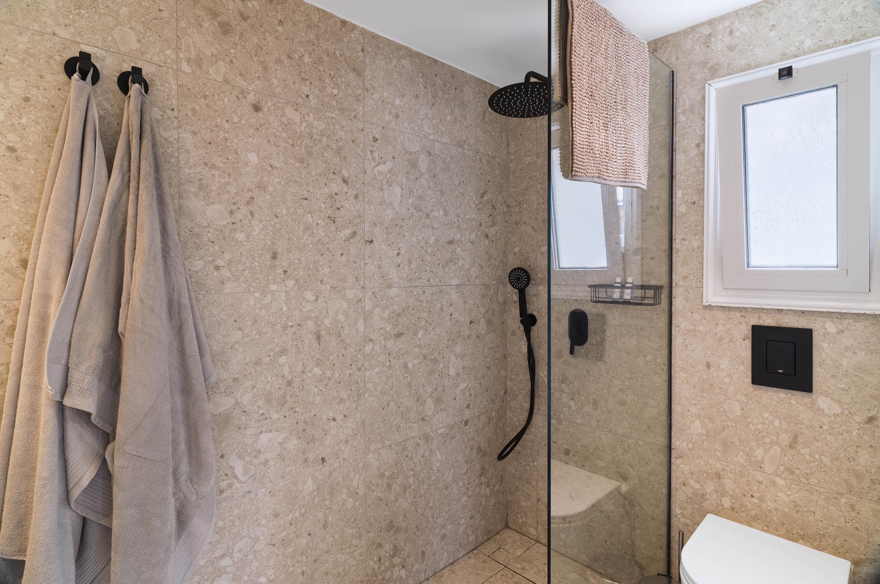 A bathroom with a glass shower enclosure, a towel rack with towels, a toilet, and a window.