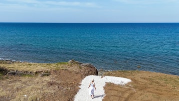 A coastal landscape with a clear sky, a rocky shoreline, and a person walking on a gravel path.
