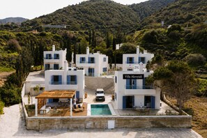Una villa moderna con piscina, rodeada de exuberante vegetación y colinas.
