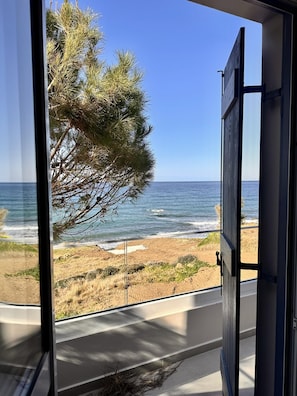 A view from a window overlooking a beach with a tree and ocean. - Villa Akroyiali Seafront (Pachyammos)
