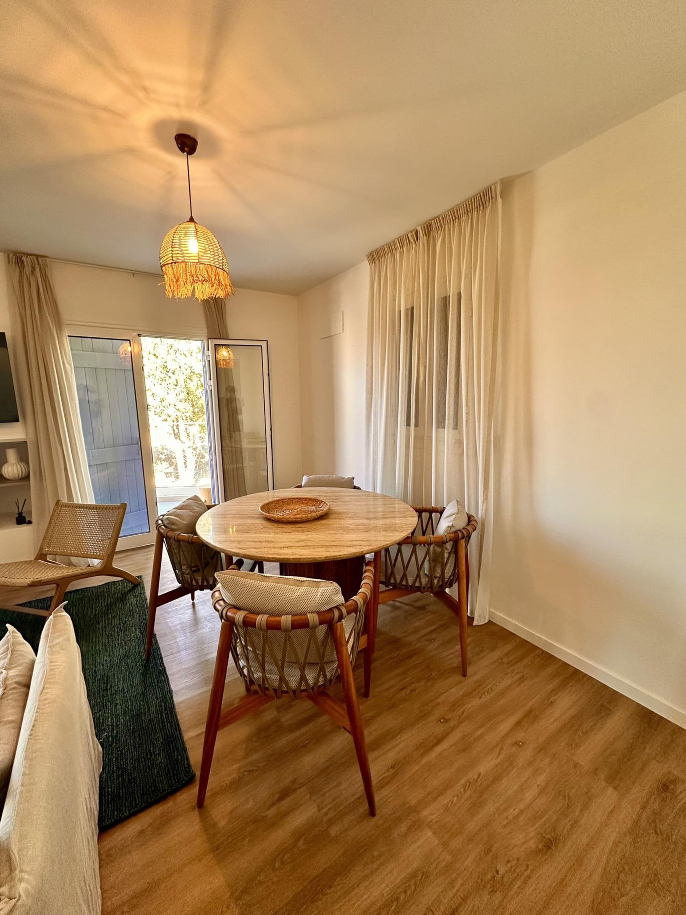Un comedor con una mesa redonda de madera, sillas de mimbre y una lámpara colgante.