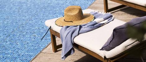 A poolside lounge chair with a straw hat and a patterned towel.