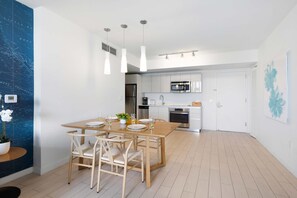 Una cocina moderna con armarios blancos, electrodomésticos de acero inoxidable y un comedor con mesa y sillas de madera.