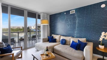 Una sala moderna con un ventanal grande, un mural de mapa, un sofá con cojines azules y una mesa de comedor con una botella y vasos.