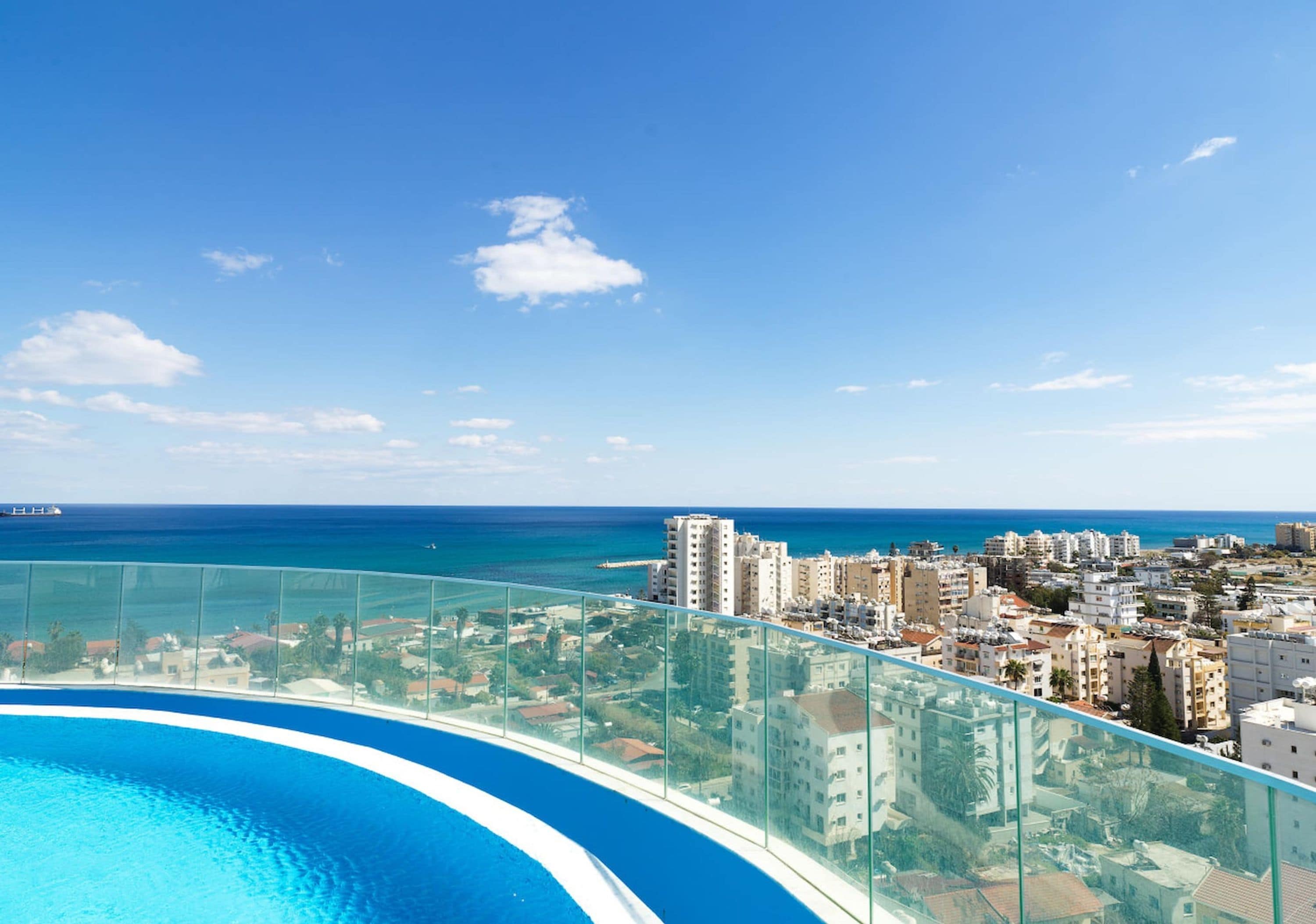 A high-rise building with a glass balcony overlooking a cityscape and the sea.