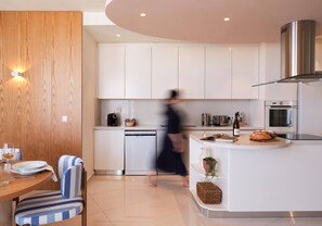 A modern kitchen with white cabinetry, a built-in dishwasher, and a stainless steel range hood. - Althea Luxury Residence (Larnaca)