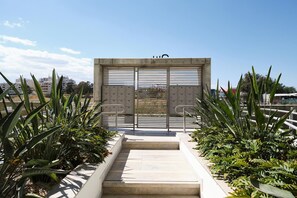 A gated entrance with a metal gate and a set of stairs leading up to it, surrounded by tropical plants. - Althea Luxury Residence (Larnaca)