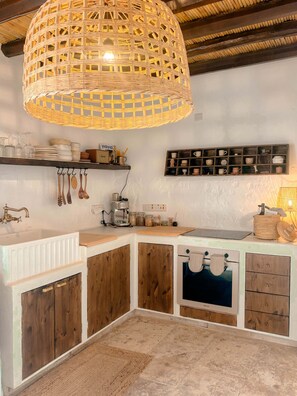 Une cuisine dotée d’un îlot central, de meubles de rangement en bois, d’un luminaire suspendu et de divers ustensiles de cuisine rangés sur des étagères.