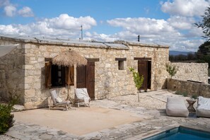 Un bâtiment en pierre doté d’une piscine, de portes en bois et d’un toit de chaume.