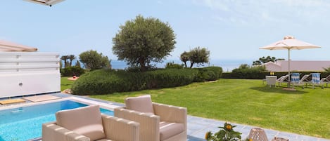 A poolside area with wicker furniture, a table with a vase of sunflowers, and a view of the sea.