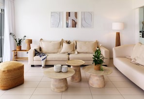 En moderne stue med en beige sofa, to runde sofaborde og et stort vindue.