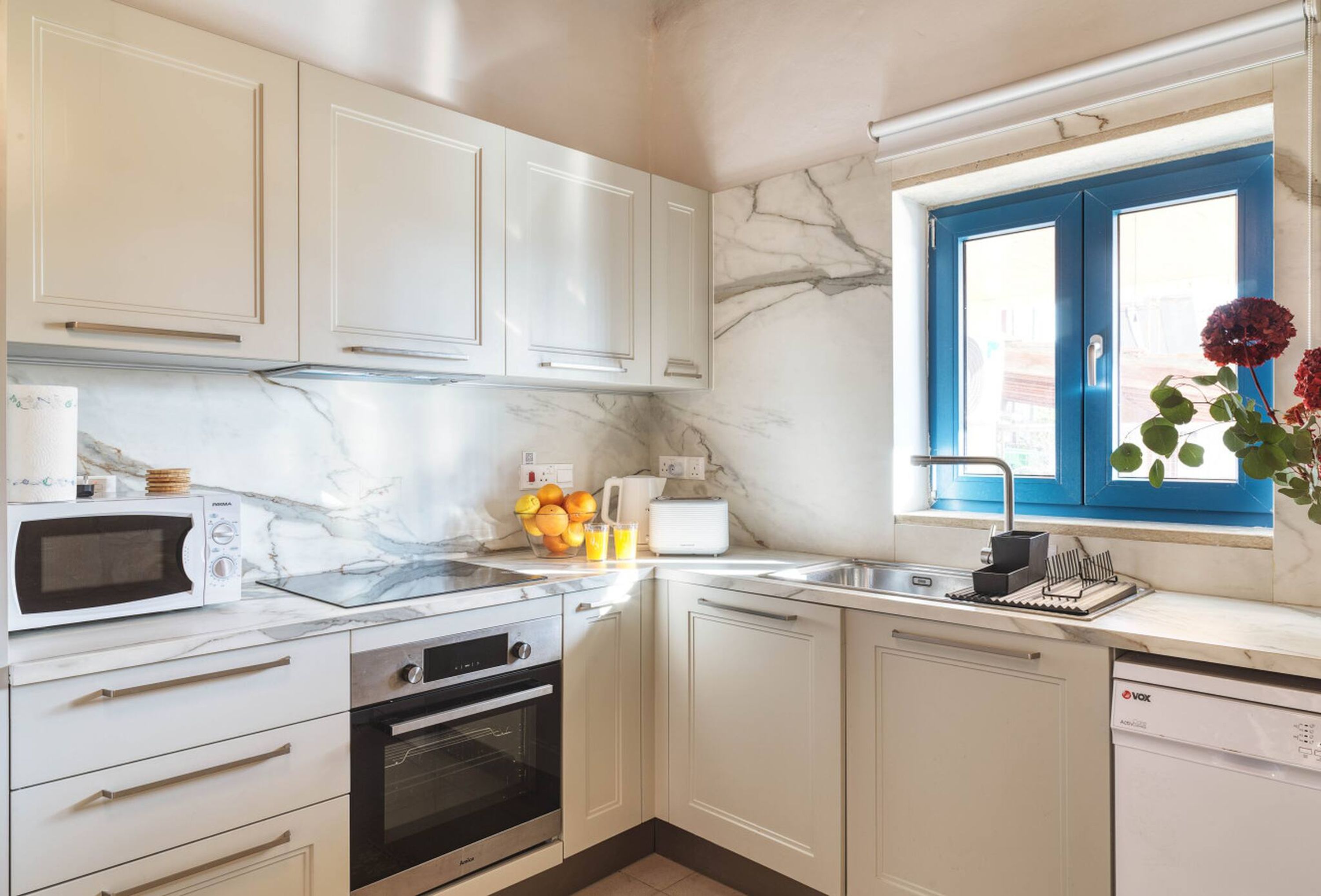 Una cocina compacta con armarios blancos, un microondas integrado, una estufa y un lavabo.