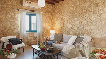 Una habitación acogedora con paredes de piedra, techo de madera, un sofá, una mesa de centro y una zona de comedor con pan y queso.