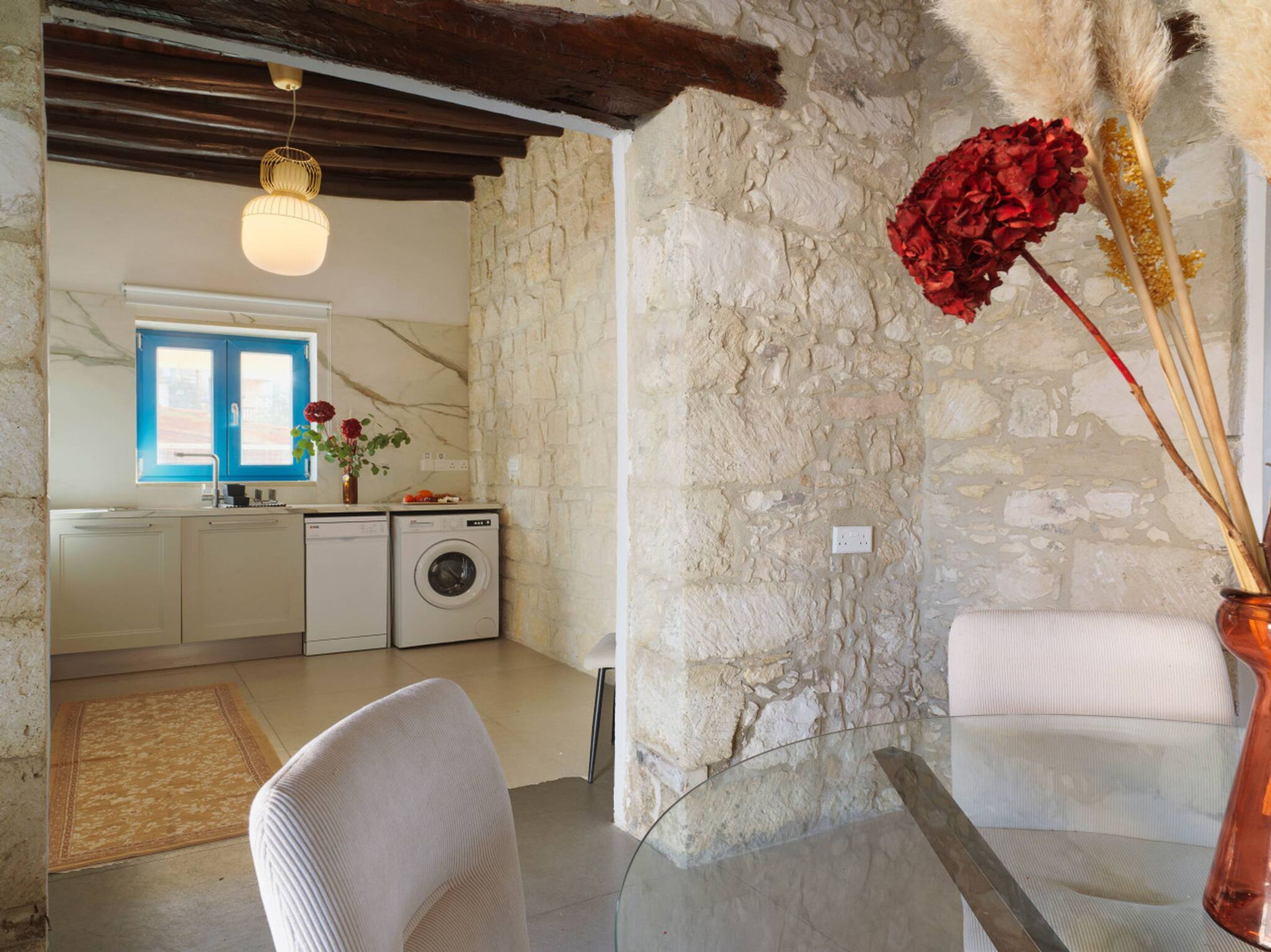 Una cocina moderna con pared de piedra, lavadora y comedor con mesa de vidrio.