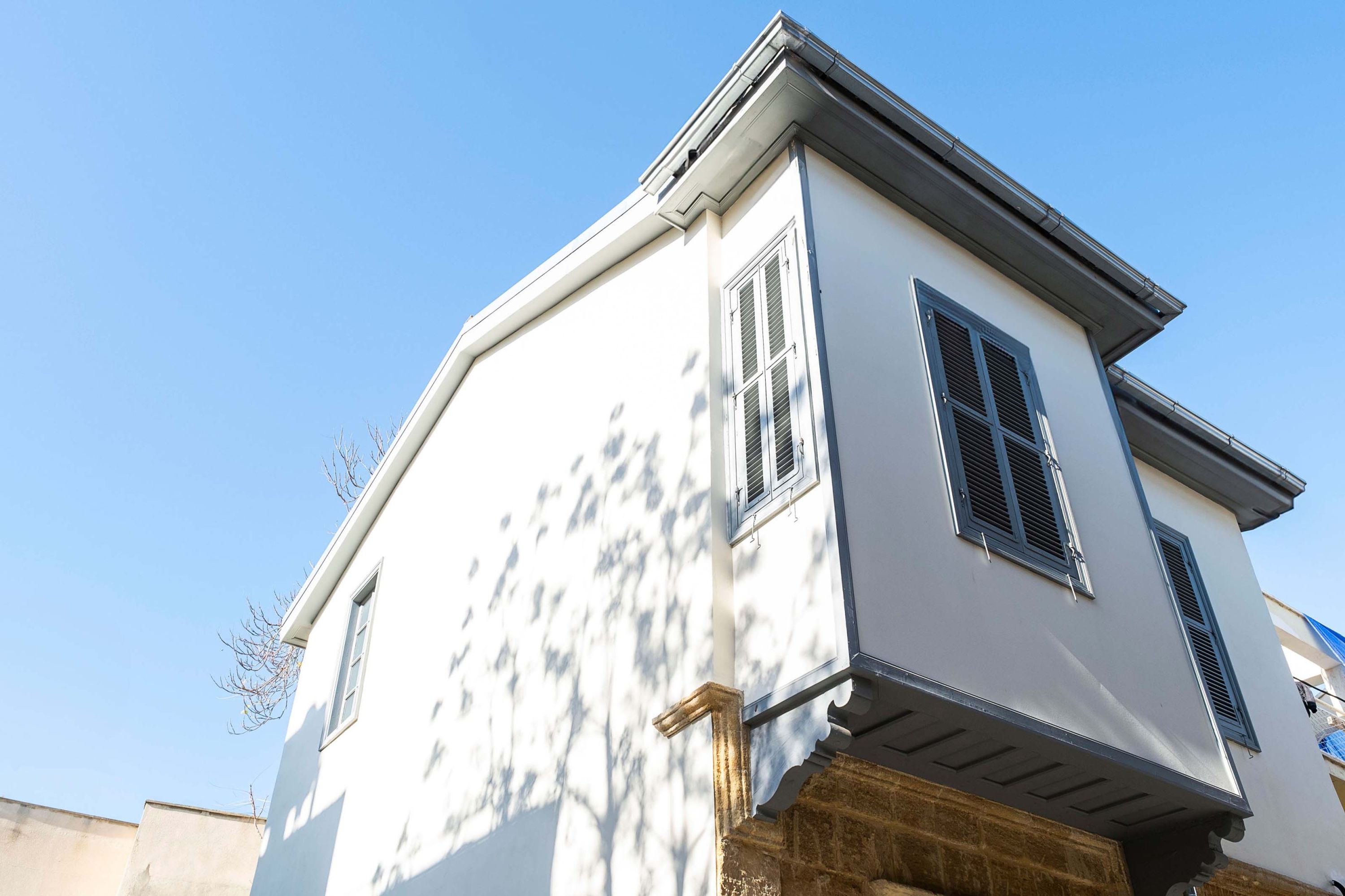 Un immeuble de deux étages avec une façade blanche et des volets sombres aux fenêtres.