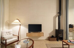 A living room with a sofa, a table with a book, a lamp, a TV, and a wood-burning stove.