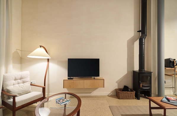 Una sala de estar con un sofá, una mesa con un libro, una lámpara, un televisor y una estufa de leña.